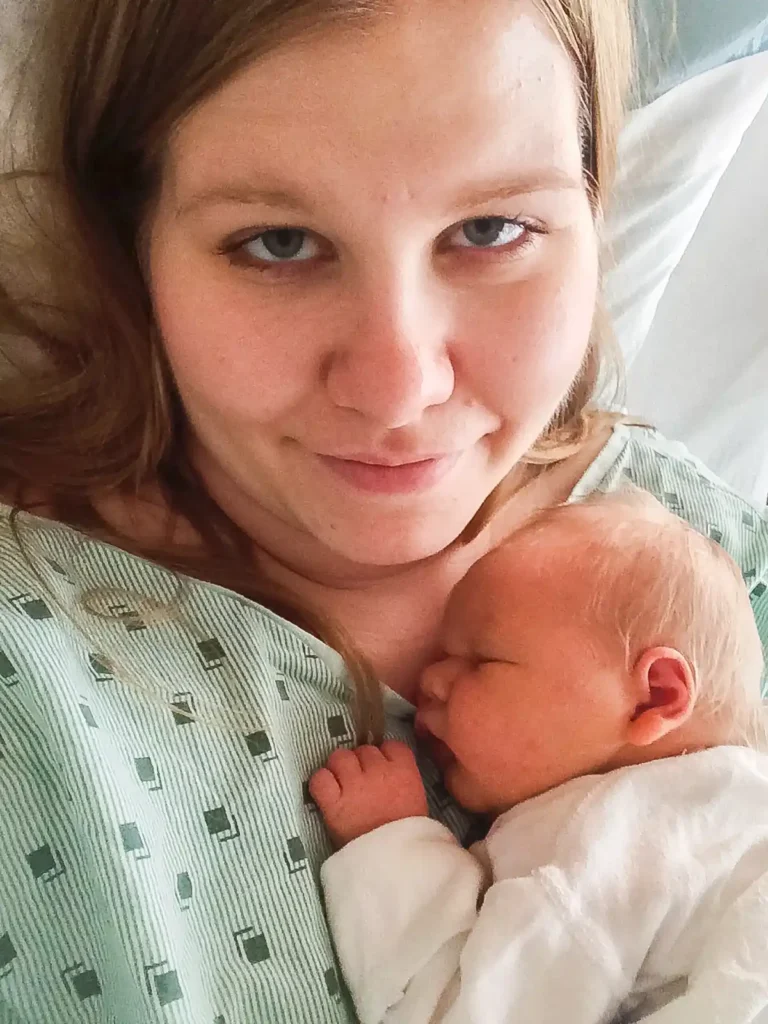 New mother cuddling her sleeping newborn baby against her chest while resting in a hospital bed after giving birth.