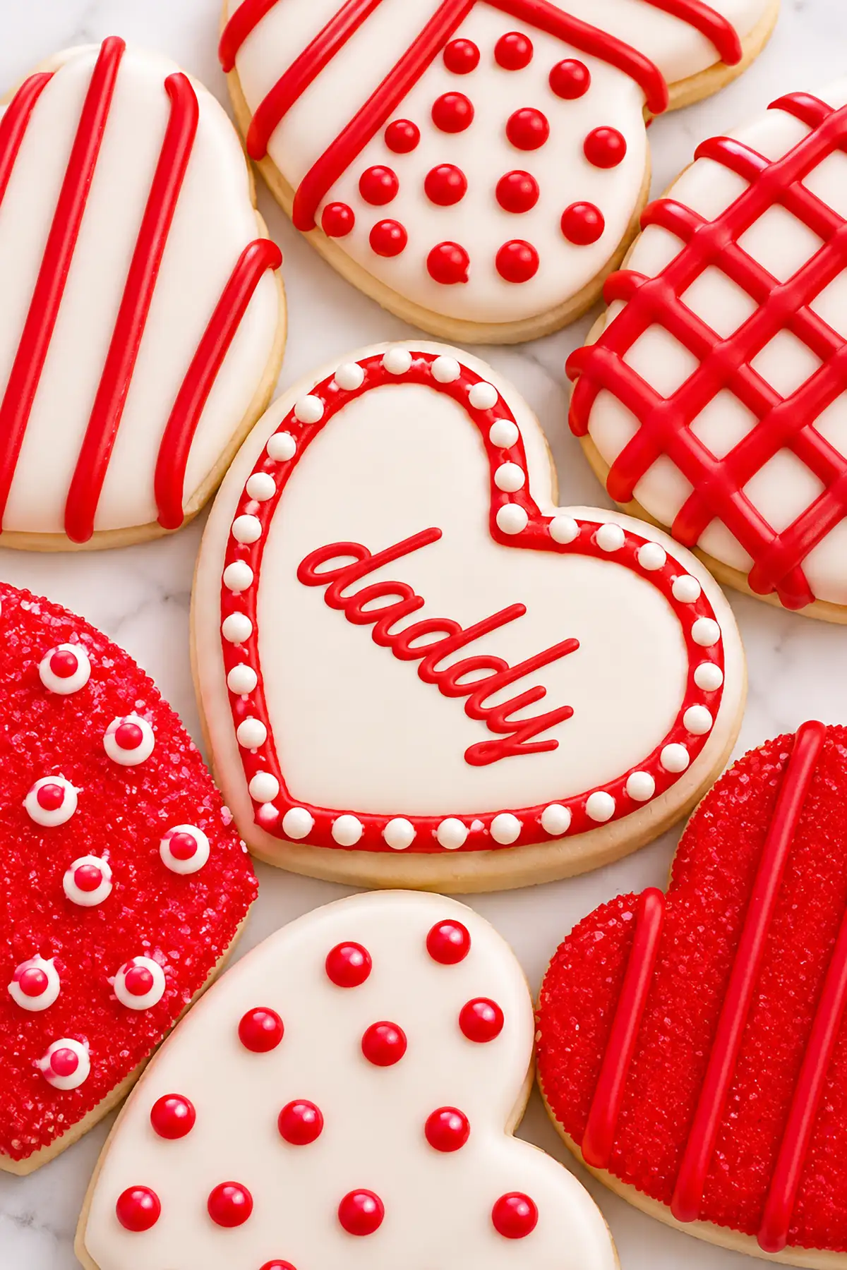 Heart-shaped Valentine's Day sugar cookies with red and white icing, including a cookie spelling "daddy" for a pregnancy announcement.