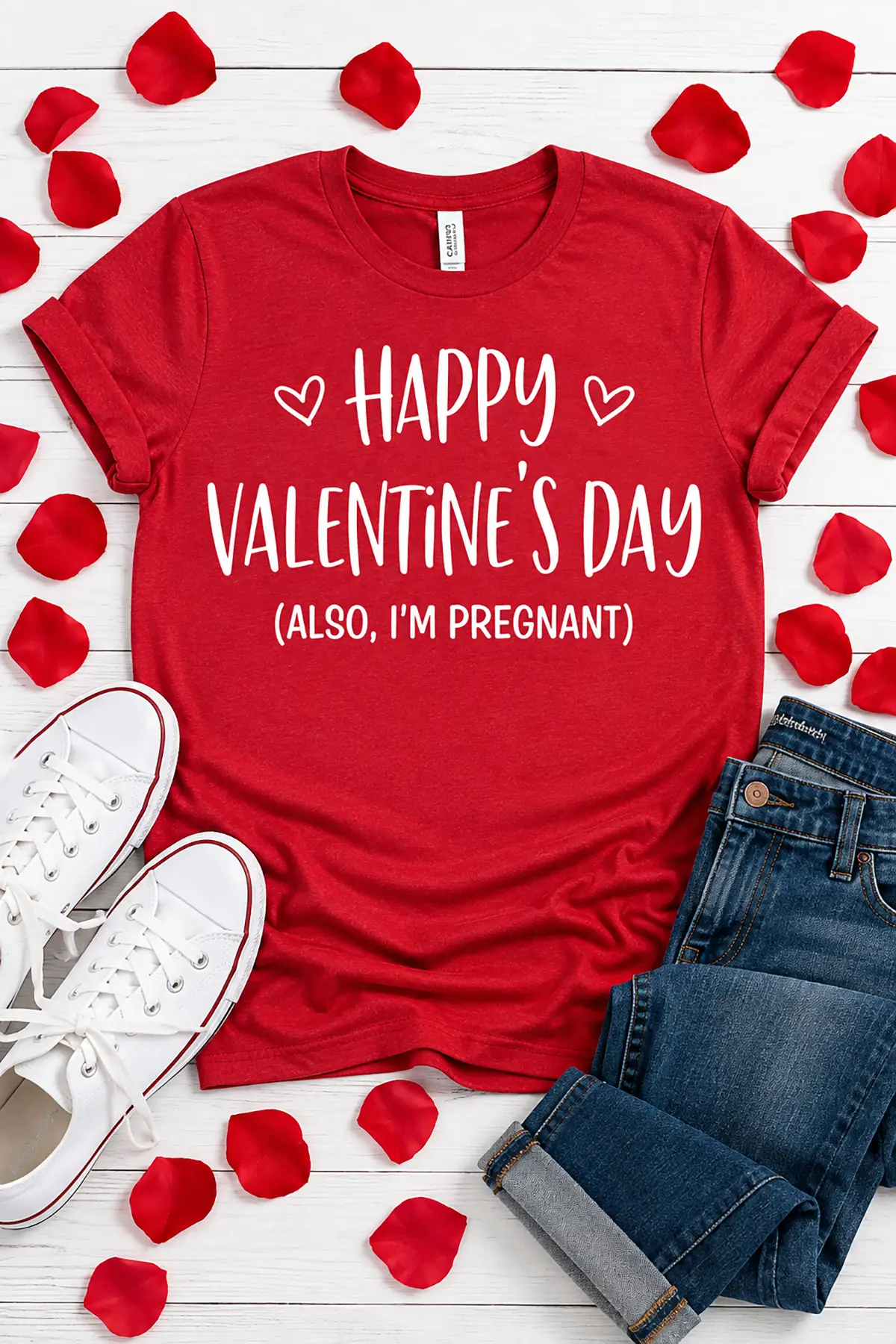 Red Valentine's Day pregnancy announcement T-shirt reading "Happy Valentine's Day (Also, I'm Pregnant)" styled with jeans and rose petals.