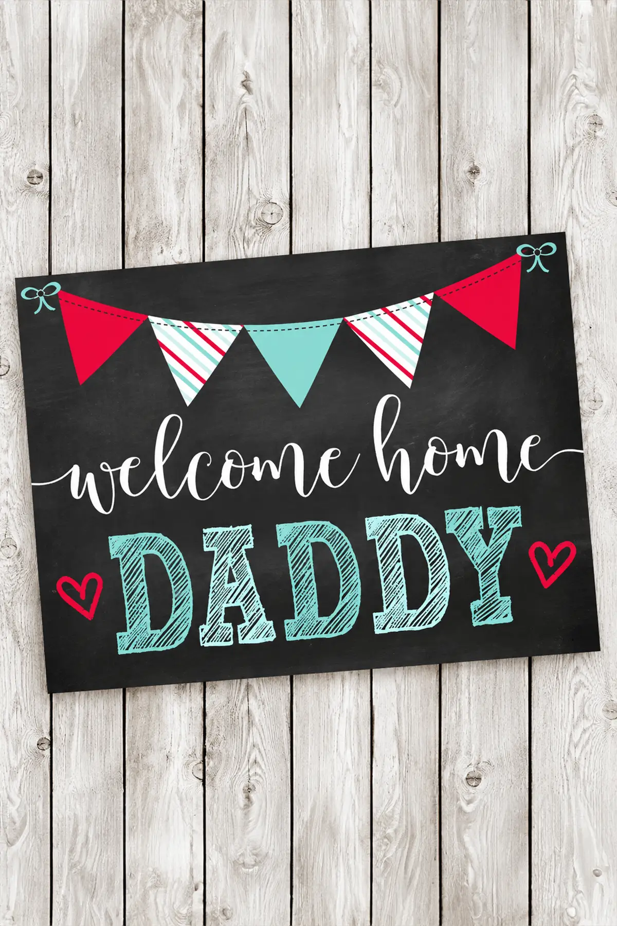 Chalkboard-style "Welcome Home Daddy" pregnancy announcement sign with colorful bunting on a rustic white wooden background.